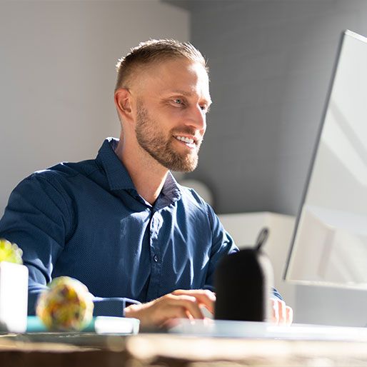 Lächelnder Mann in Büro oder Homeoffice arbeitet an einem Computerbildschirm.